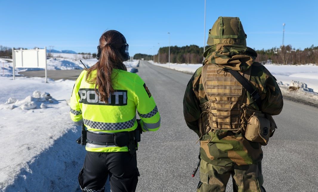 En politibetjent og militær med ryggen mot kamera i vinterlandskap 