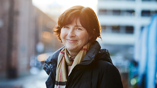 En middelaldrende dame som ser inn i kamera og smiler. Foto.